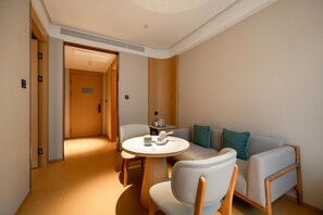 A hotel room with a round table, two chairs, a sofa, and a door leading to another room. - Ji Hotel Guangzhou Huadu Square Metro Station (Guangzhou)
