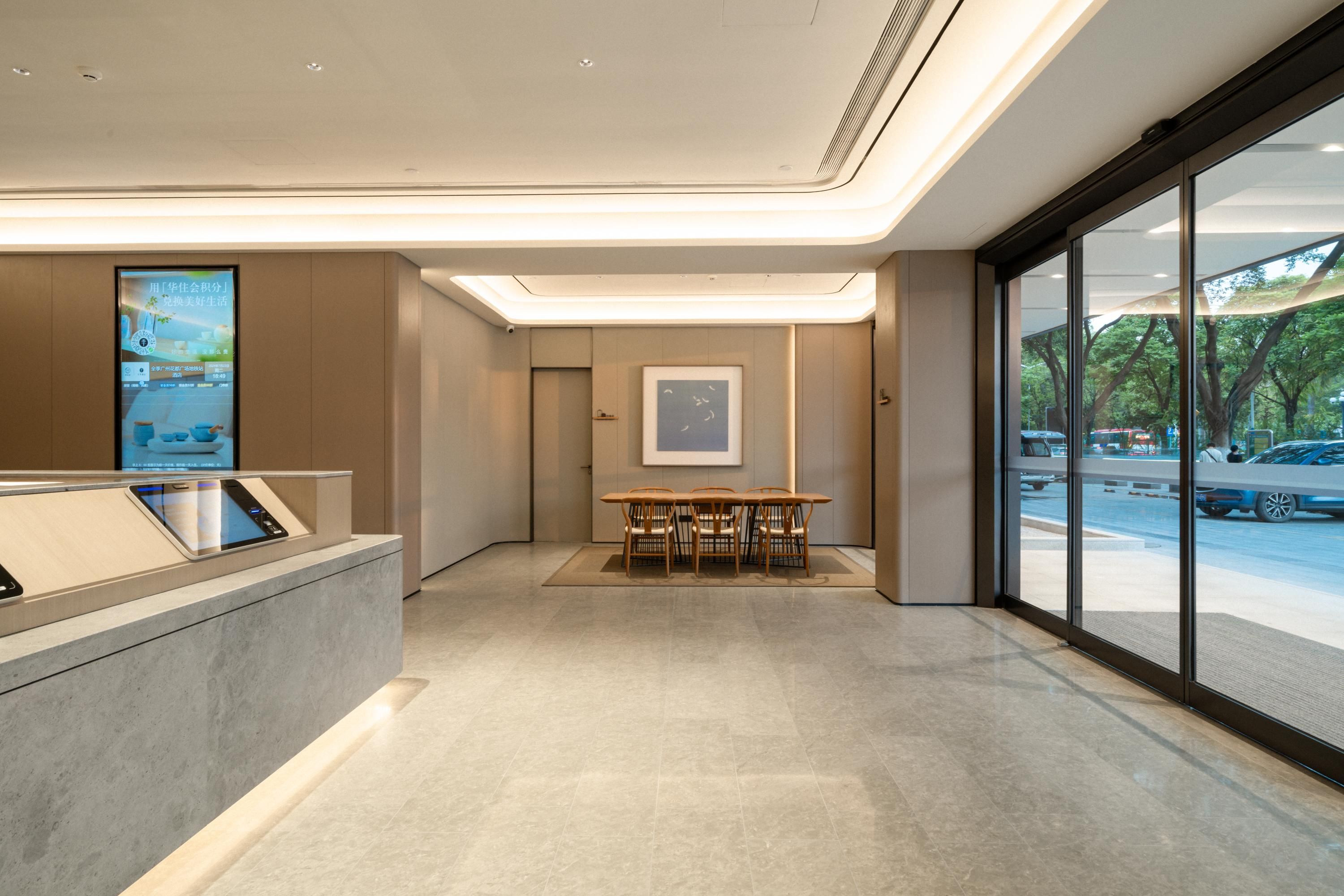 Un moderno vestíbulo de hotel con mostrador de recepción, zona de estar con sillas y amplios ventanales con vistas a la calle.