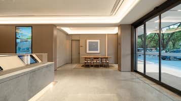 Un moderno vestíbulo de hotel con mostrador de recepción, zona de estar con sillas y amplios ventanales con vistas a la calle.