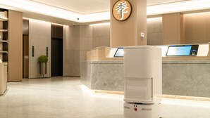 A modern hotel lobby with a reception desk, a digital kiosk, and a security camera on the ceiling. - Ji Hotel Guangzhou Huadu Square Metro Station (Guangzhou)