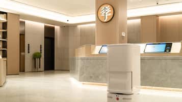 Un lobby moderno de hotel con un mostrador de recepción, un quiosco digital y una cámara de seguridad en el techo.