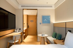 A hotel room with a bed, a desk, a chair, a small table, a TV, a painting, and a door leading to a bathroom. - Ji Hotel Guangzhou Huadu Square Metro Station (Guangzhou)