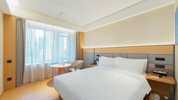 Una habitación de hotel con una cama grande, una mesita de noche con lámpara, una pequeña mesa redonda y una silla.