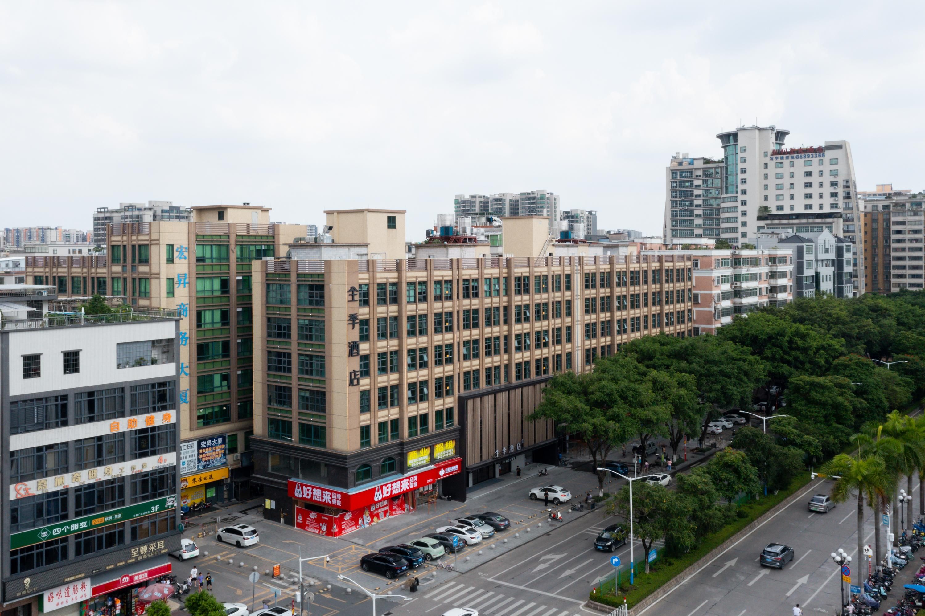 Un edificio de varios pisos con locales comerciales en la planta baja, rodeado de un estacionamiento y una calle con automóviles.