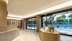 A modern reception area with a curved reception desk, a large glass door leading outside, and a view of the street and greenery. - Ji Hotel Guangzhou Huadu Square Metro Station (Guangzhou)