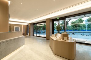 A modern reception area with a curved reception desk, a large glass door leading outside, and a view of the street and greenery. - Ji Hotel Guangzhou Huadu Square Metro Station (Guangzhou)