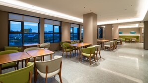 A modern dining area with tables and chairs, large windows with city views, and a green seating area. - Ji Hotel Guangzhou Huadu Square Metro Station (Guangzhou)