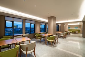 A modern dining area with tables and chairs, large windows with city views, and a green seating area. - Ji Hotel Guangzhou Huadu Square Metro Station (Guangzhou)