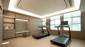 Une salle de sport moderne équipée de deux tapis de course, d’une petite table avec des bouteilles d’eau et offrant une vue sur la ville grâce à de grandes fenêtres.