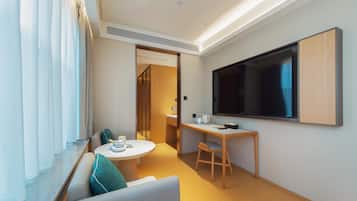 Una habitación de hotel moderna con un sofá, una mesita redonda pequeña, un escritorio y un televisor montado en la pared.