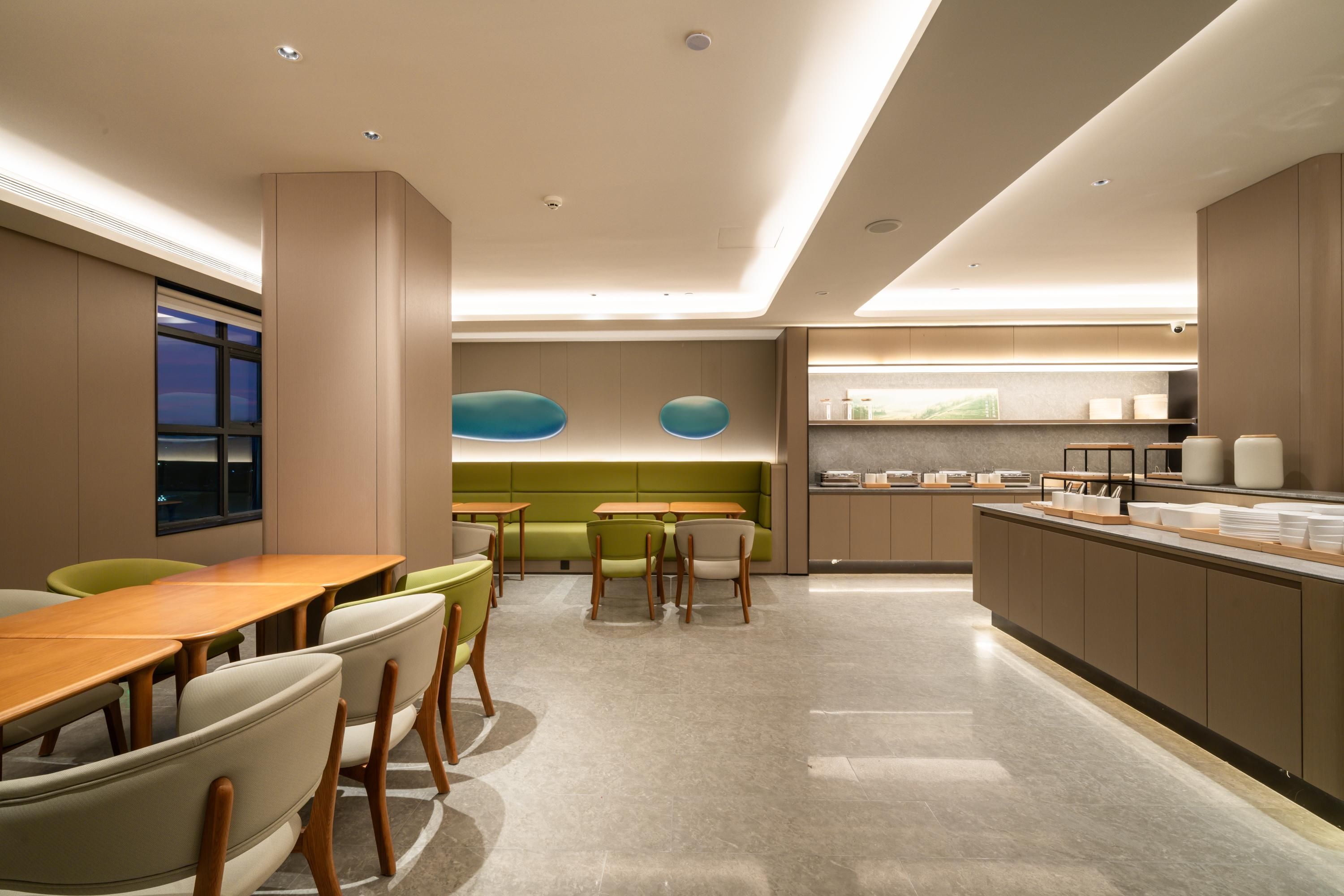 A modern dining area with a long wooden table and chairs, a green sofa, and a kitchen counter with various items.