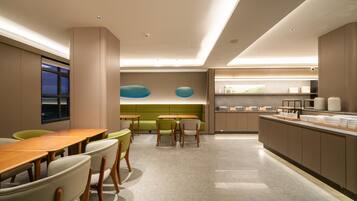 A modern dining area with a long wooden table and chairs, a green sofa, and a kitchen counter with various items.