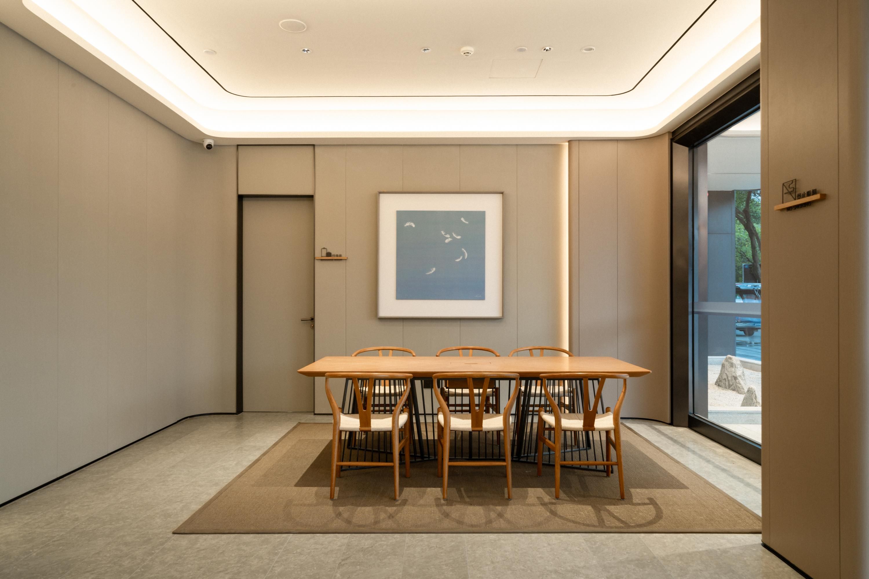 Uma sala de conferência moderna com uma mesa comprida e cadeiras, uma obra de arte emoldurada na parede e vista através de uma porta de vidro.