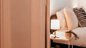 A bedroom with a bed, bedside table, lamp, and wall-mounted picture frames.