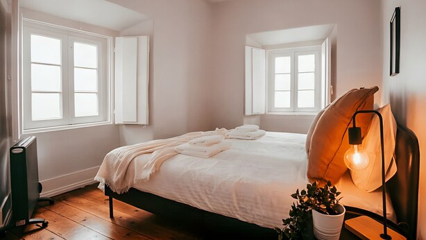 A bedroom with a bed, a bedside lamp, a radiator, and windows.