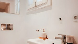 A modern bathroom with a white sink, toilet, and a window above the sink.