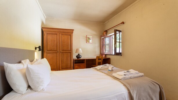 Habitación de hotel con una cama grande, un armario de madera, un escritorio con lámpara y una ventana con cortinas.