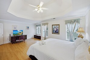 A hotel room with a bed, a desk, a chair, a ceiling fan, and a television.