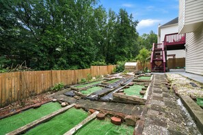 Un jardin à l’arrière de la maison, avec des plates-bandes surélevées, une clôture en bois et une maison dont le garde-corps est rouge.