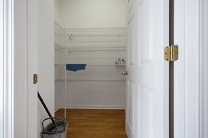 Un couloir avec un seau et une serpillière, un espace douche avec une serviette, et une porte dotée d’un loquet.