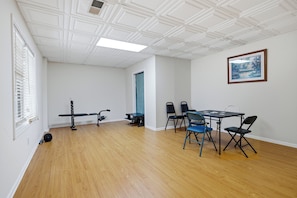 Une pièce avec un plancher en bois, des murs blancs, un plafond orné d’un motif en réseau, un banc, une table avec des chaises et un tableau encadré accroché au mur.