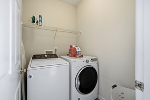 A laundry room with two Whirlpool washers, a shelf with cleaning products, and a basket.