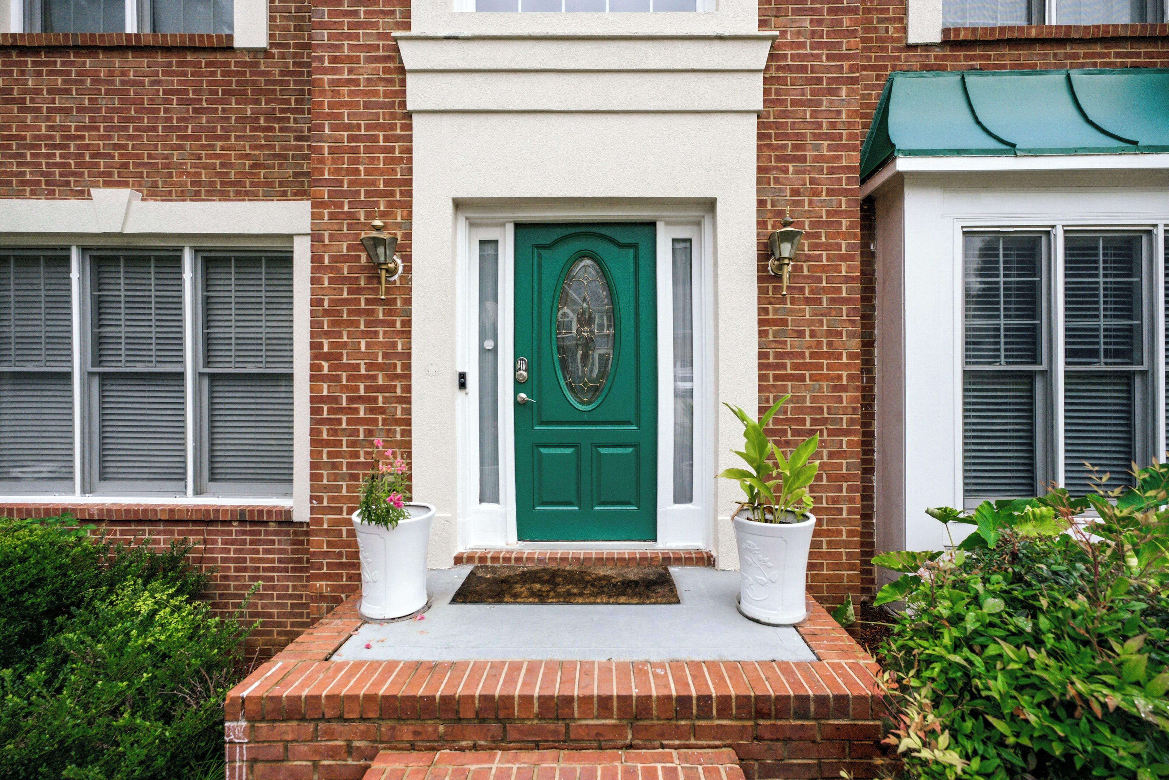 A brick house with a green door, two potted plants, and a small brick step leading to the entrance.
