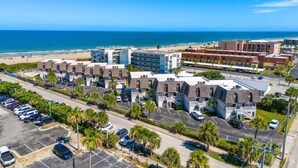 Un hotel costero con varias construcciones, un estacionamiento y una playa al fondo.