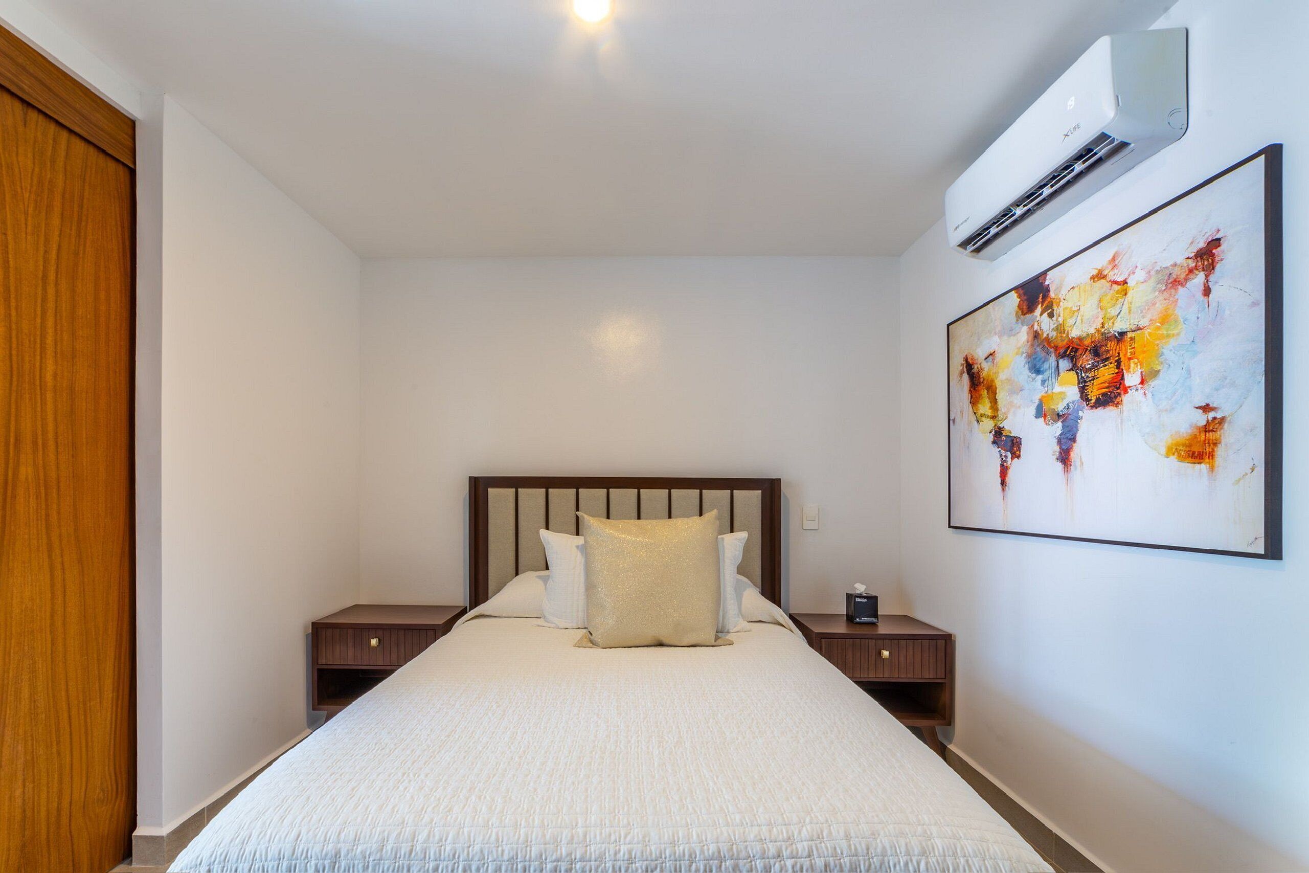 Ein Hotelzimmer mit einem großen Bett, einem Holz-Kopfteil, einem Nachttisch und einer Wandklimaanlage.