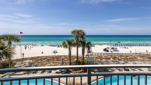 A beach view with a pool area, palm trees, and a flag.