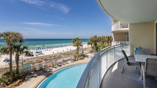 A balcony with a view of a beach, a pool, and a pier in the distance.