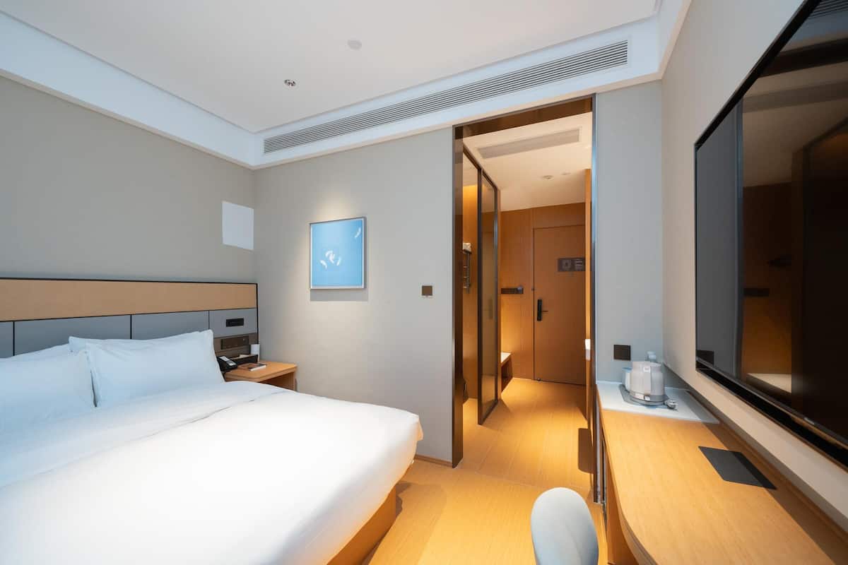 A hotel room with a large bed, bedside table, and a mirror.