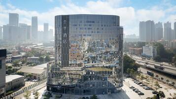 Un edificio moderno y cilíndrico con fachada de vidrio, rodeado de un estacionamiento y calles urbanas.