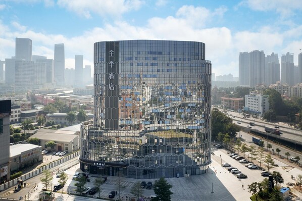 A modern, cylindrical building with a glass facade, surrounded by a parking lot and urban streets. - Ji Hotel Guangzhou Panyu Chimelong Wanbo (Guangzhou)