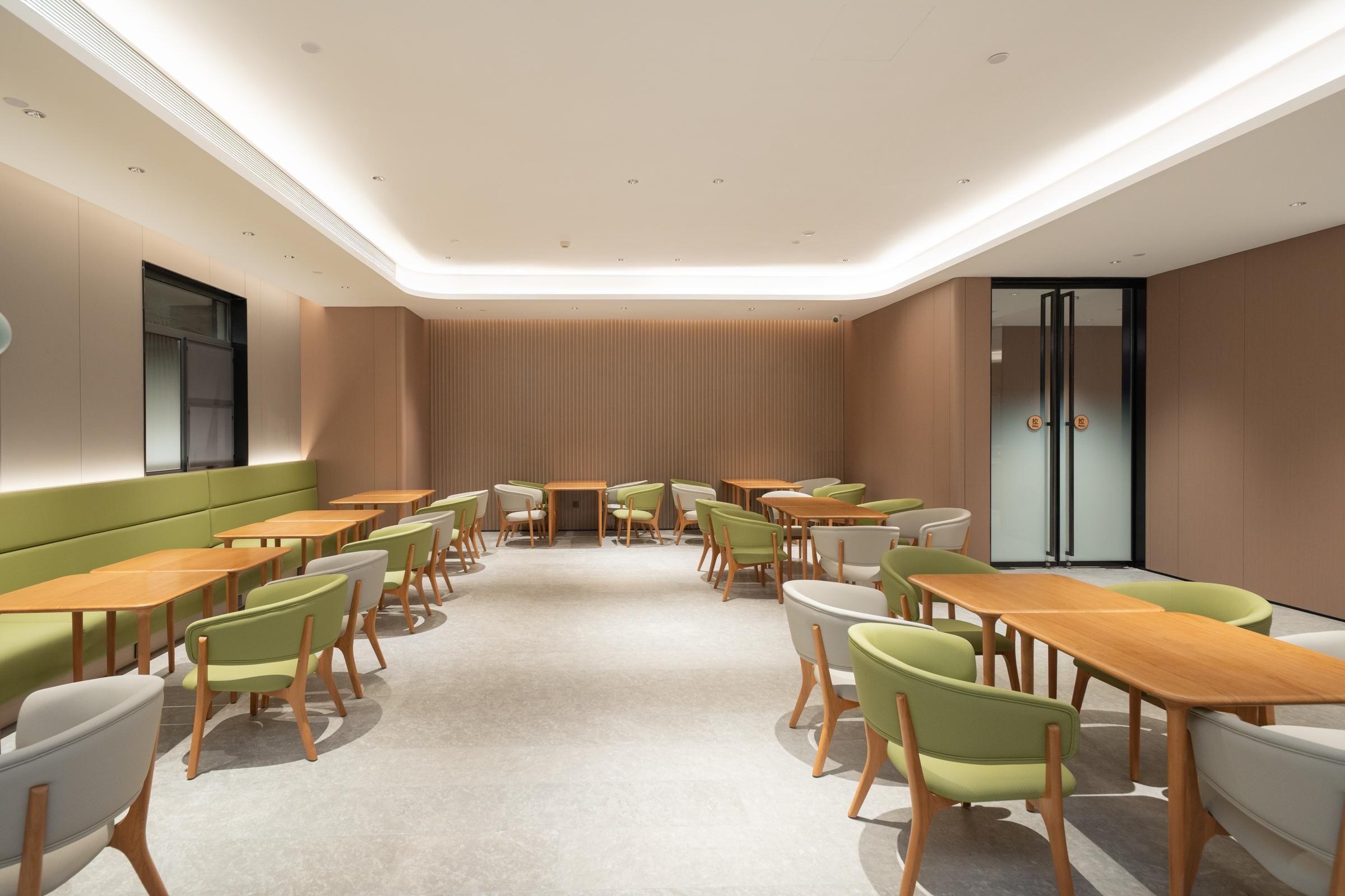 Een moderne vergaderruimte met een lange tafel, meerdere stoelen en een groene, beklede bank langs een muur.