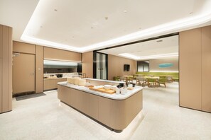 A modern kitchen with a central island, built-in appliances, and a dining area with green chairs. - Ji Hotel Guangzhou Panyu Chimelong Wanbo (Guangzhou)
