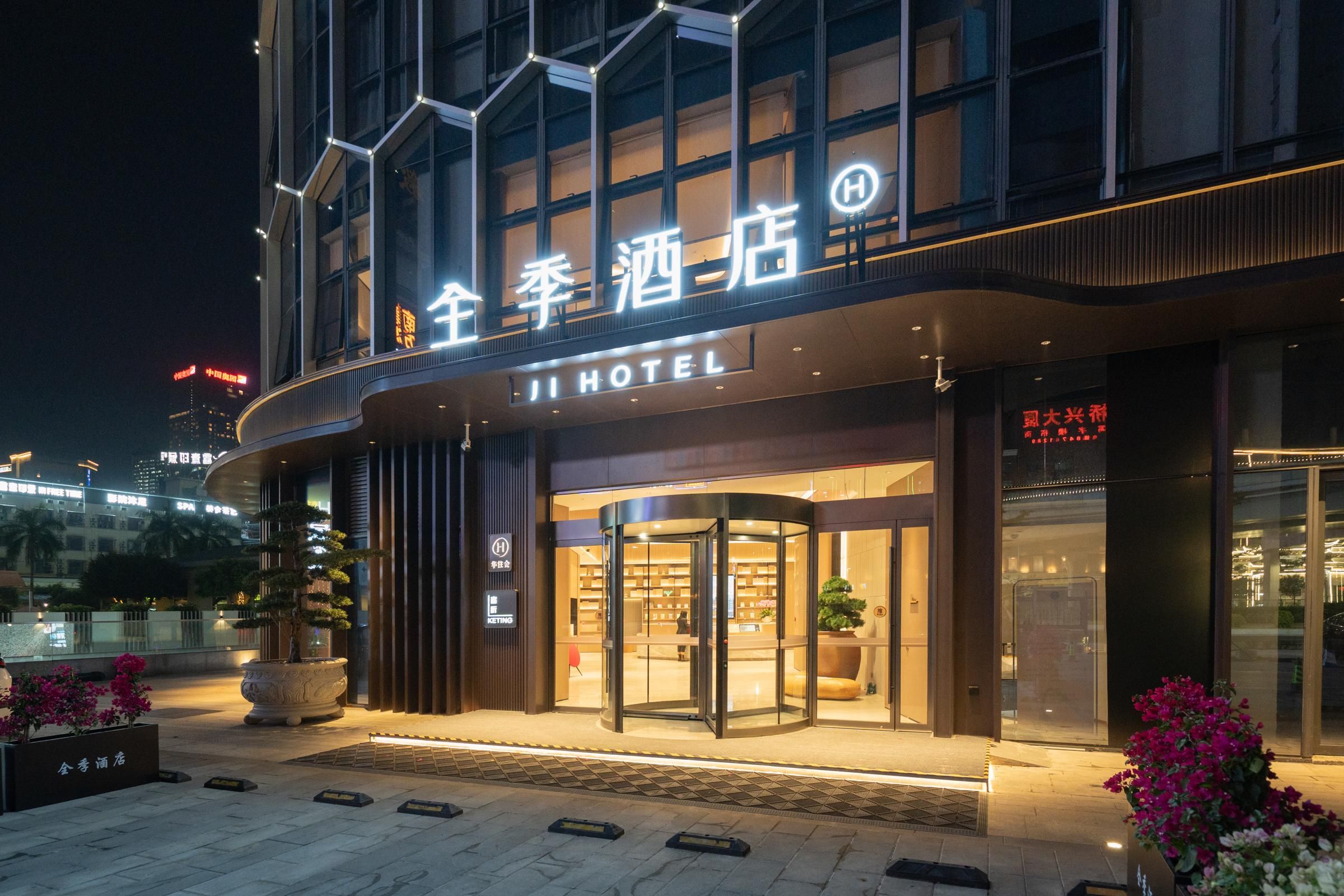 Een hotel ingang met een draaideur, verlichte signage en potplanten.