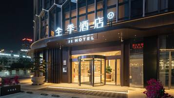 Een hotel ingang met een draaideur, verlichte signage en potplanten.