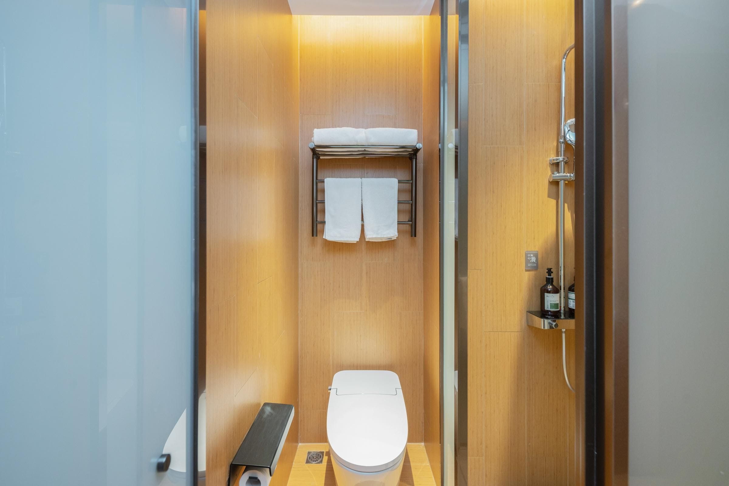 A compact, modern bathroom with a wooden vanity, a toilet, and a shower area.