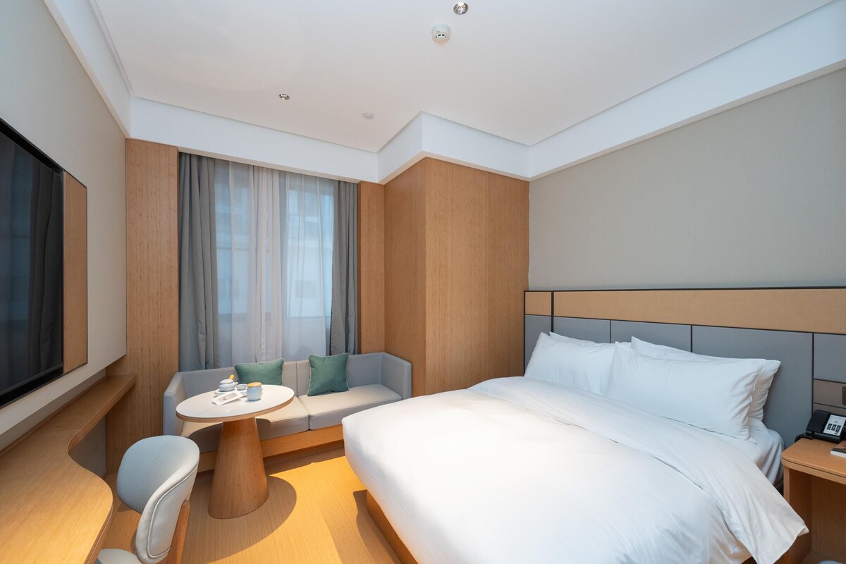 A modern hotel room with a large bed, a small round table, a sofa, and a TV.