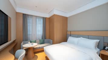 Quarto de hotel moderno com uma cama grande, uma mesa redonda pequena, um sofá e uma televisão.