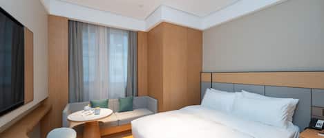 Una habitación de hotel moderna con una cama grande, una mesita redonda, un sofá y un televisor.