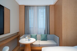 Une chambre d’hôtel moderne avec un canapé, une petite table ronde et un téléviseur fixé au mur.