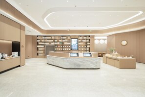 A modern hotel lobby with a central reception desk, a large digital display, and a seating area with tables and chairs. - Ji Hotel Guangzhou Panyu Chimelong Wanbo (Guangzhou)