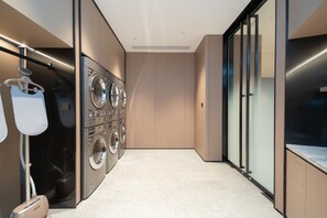 A modern laundry room with a washing machine and dryer, a drying rack, and a towel dispenser.