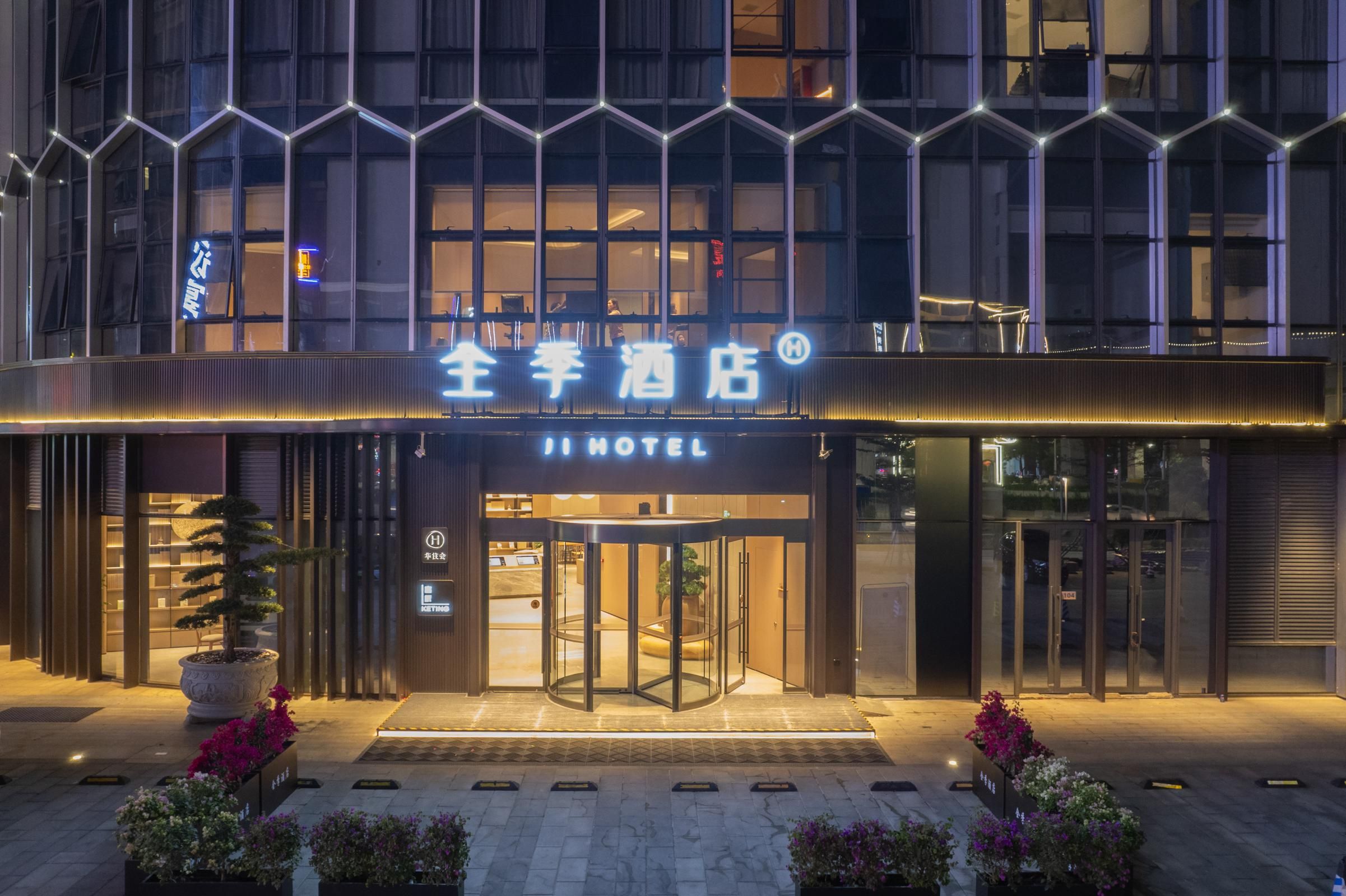A hotel entrance with a revolving door, illuminated signage, and potted plants.
