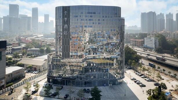 A modern, cylindrical building with a glass facade, surrounded by a parking lot and urban streets. - Ji Hotel Guangzhou Panyu Chimelong Wanbo (Guangzhou)