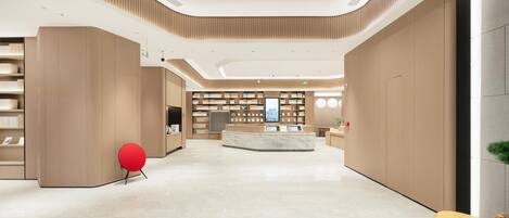 A modern lobby with a central reception desk, bookshelves, and a red chair.