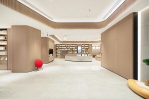 A modern lobby with a central reception desk, bookshelves, and a red chair. - Ji Hotel Guangzhou Panyu Chimelong Wanbo (Guangzhou)