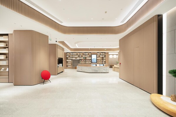 A modern lobby with a central reception desk, bookshelves, and a red chair.